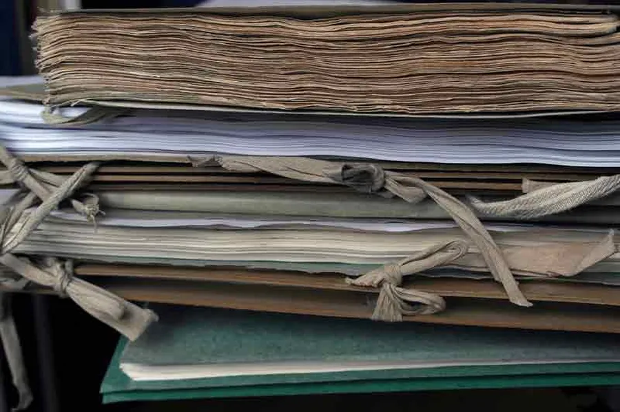 Side view of a pile of working materials: music volumes and gray folders tied together with ribbons.